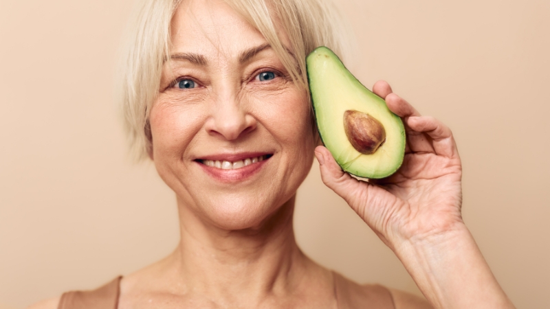 Nasmejana žena drži polovinu avokada pored lica