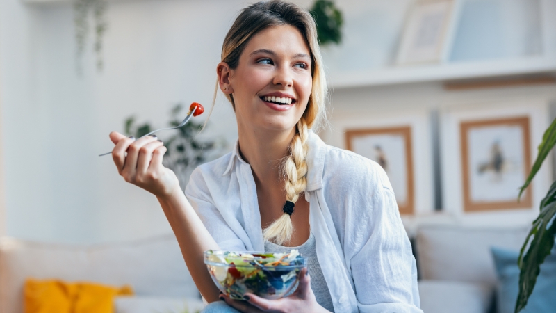 Nasmejana žena jede svežu salatu u dnevnom boravku
